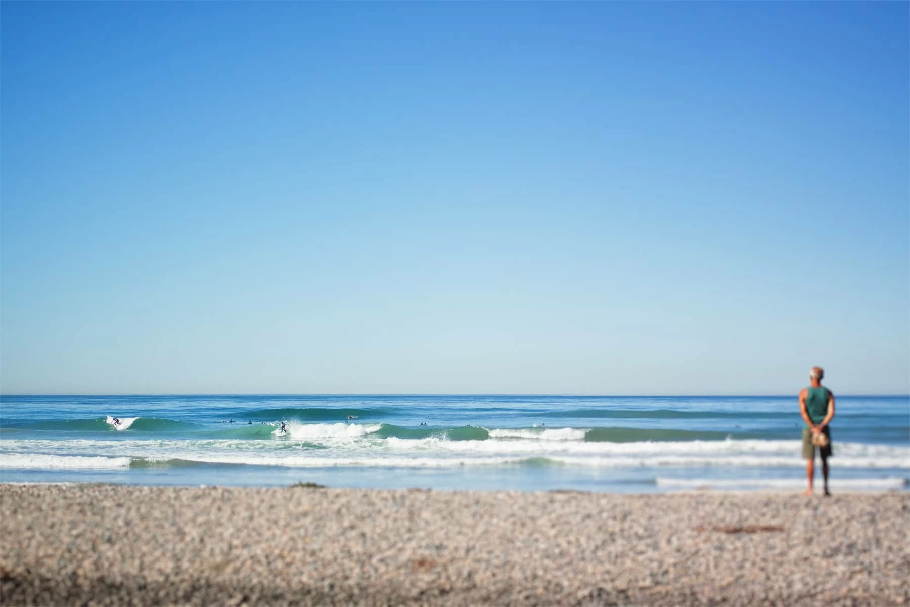 A peaceful moment on Del Mar beach as a man observes surfers catching waves.